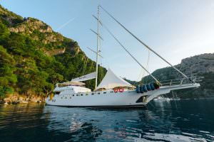 Belgin Sultan motor sailor anchored in scenic coastal bay with mountains and clear water, luxury yacht charter experience