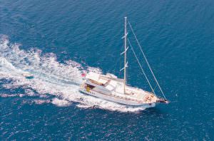 Belgin Sultan motor sailor top view cruising in deep blue sea with tender boat, luxury yacht charter experience