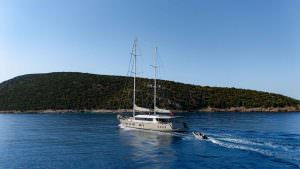 De Love motor sailer cruising in calm sea with tender boat, ultra luxury yacht charter experience near scenic coastline
