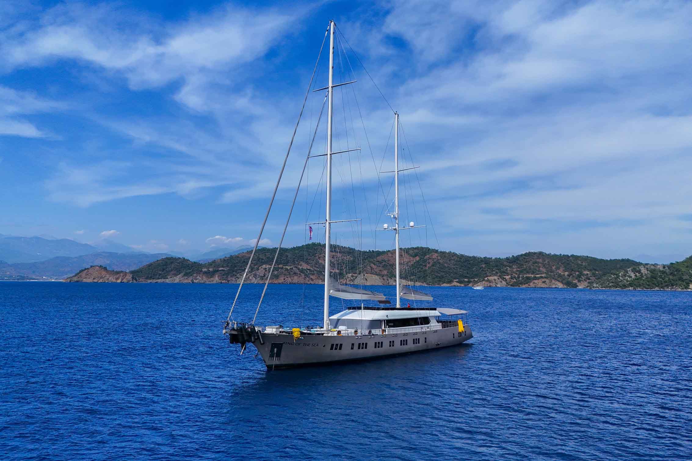 King of the Sea yacht charter motor sailer exterior profile view, luxury yacht sailing in crystal clear Mediterranean waters with elegant twin mast design