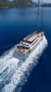 North Wind motor sailer aerial aft view, luxury yacht cruising along scenic coastline with crystal clear waters and premium charter experience