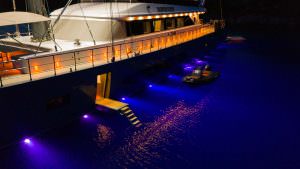 North Wind motor sailer night exterior, luxury yacht illuminated at sea with underwater lights, elegant deck lighting and tender alongside